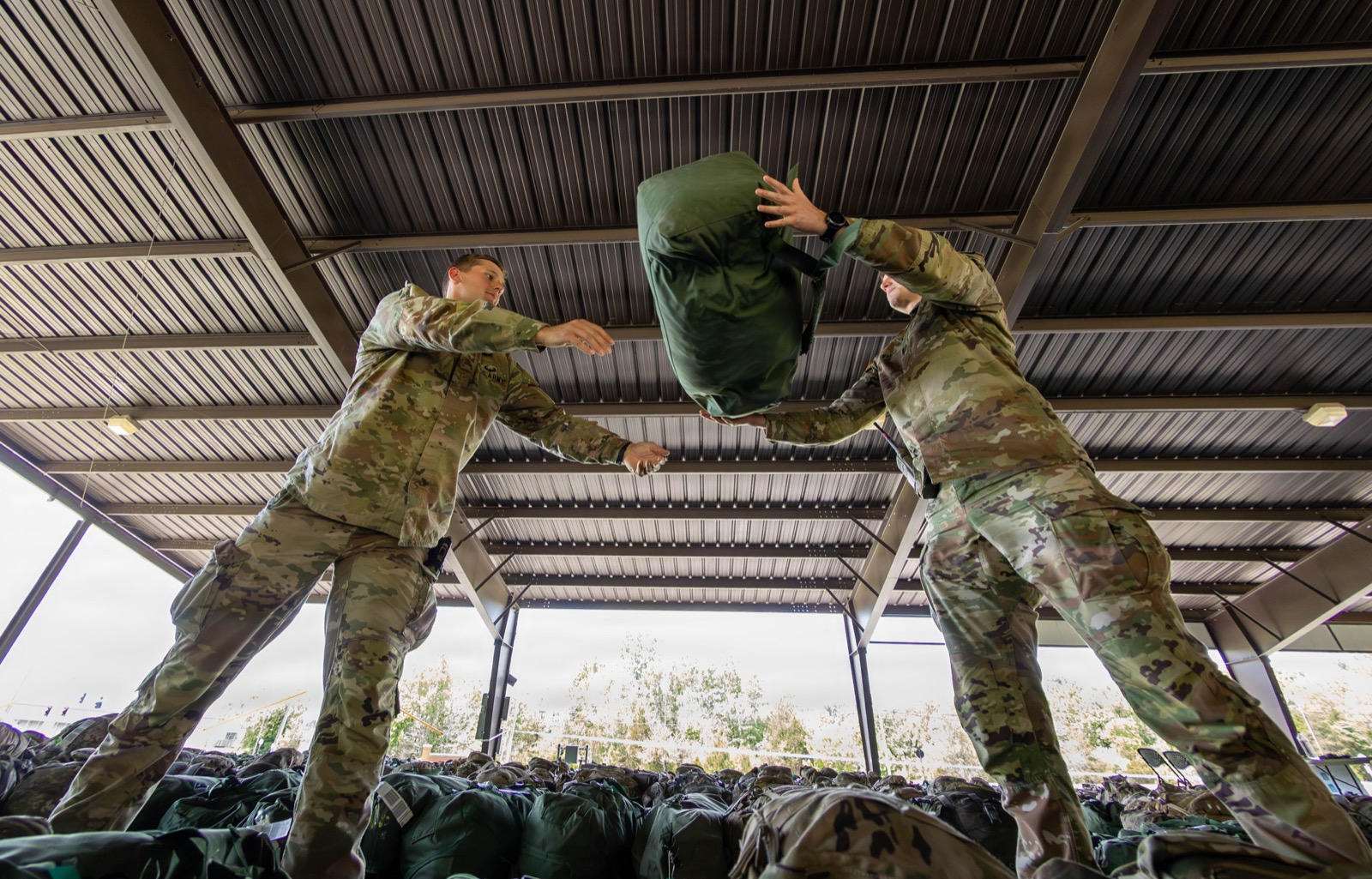 Two soldiers stacking duffel bags into an orderly pile