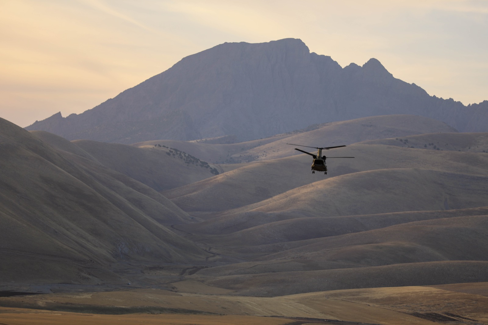 Helicopter flying low over rolling plains toward a mountain range